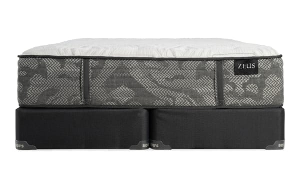 Zeus brand mattress with a gray patterned fabric side and white quilted top, resting on a black supportive base.