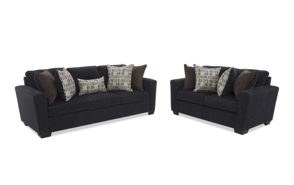Dark gray fabric living room sofa set with a three-seater and a two-seater couch, featuring multiple patterned and solid throw pillows, modern design.