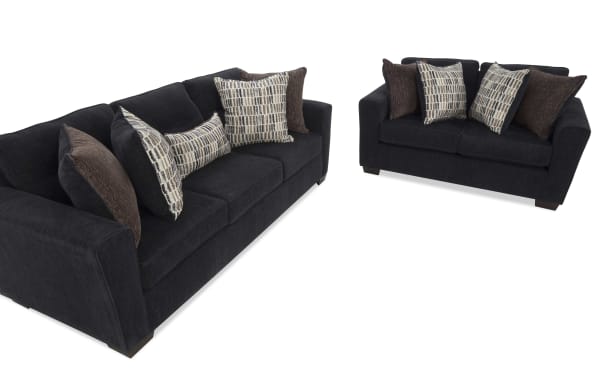 Two dark gray fabric sofas with wide arms, wooden legs, and decorative brown and patterned throw pillows, ideal for modern living rooms.