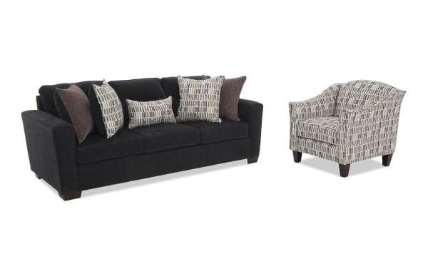 Dark gray fabric sofa with three seat cushions and six decorative pillows in patterned and solid brown tones, paired with a matching patterned fabric armchair with dark wooden legs.