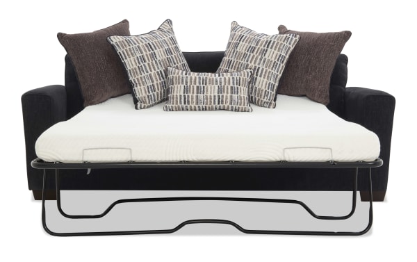 Black fabric sofa bed with a white mattress and five decorative pillows in brown and patterned beige tones, featuring a metal frame for mattress support.
