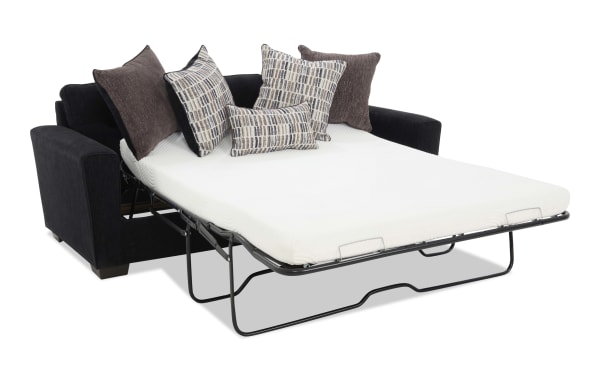 Black fabric sofa bed with a white mattress and four decorative pillows in brown and patterned fabric, featuring a fold-out metal frame for easy conversion.