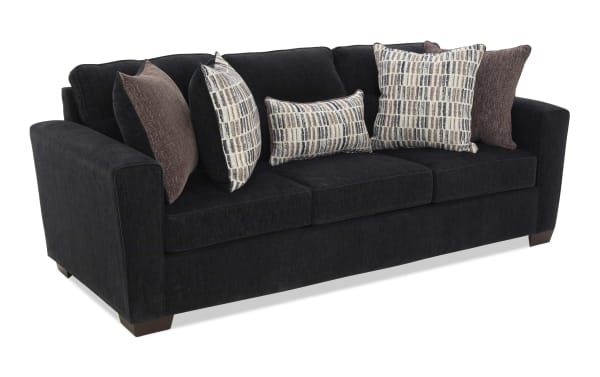 Black fabric sofa with three seat cushions and six decorative pillows in brown and patterned beige, featuring wide armrests and wooden legs, suitable for living room seating.
