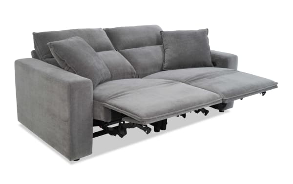 Gray fabric reclining sofa with two extended footrests, plush cushions, and wide armrests, designed for modern living room comfort.