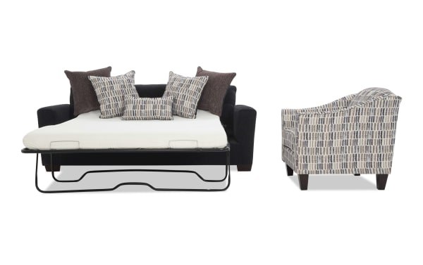 Black fabric sofa bed with metal frame, extended mattress, and multiple patterned and solid brown throw pillows; next to a patterned fabric armchair with wooden legs.