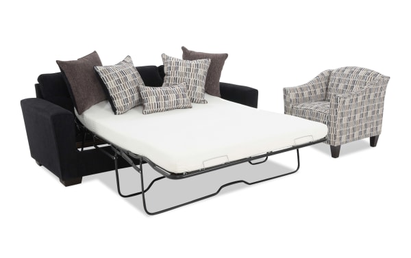 Black fabric sofa bed with metal frame mattress extended, featuring multiple patterned and solid throw pillows, next to a matching patterned armchair.