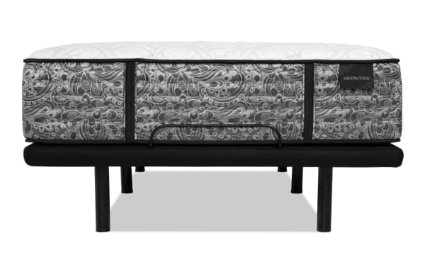 Mattress with a white quilted top and gray paisley-patterned sides on a black metal bed frame with legs, labeled "DISTINCTION."
