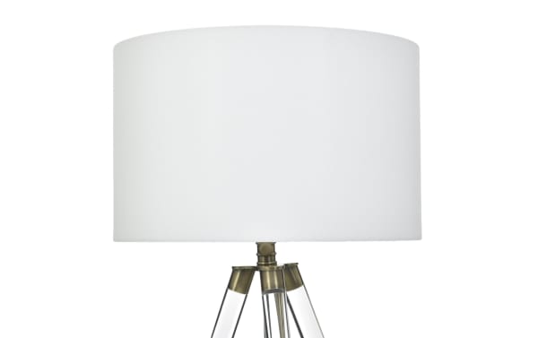 White fabric drum lampshade on a tripod lamp base with clear acrylic legs and antique brass accents, modern table lamp design.