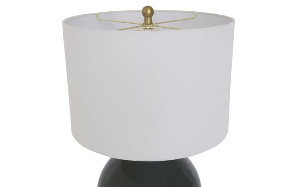 Table lamp with a white fabric drum lampshade and a brass finial, featuring a glossy black ceramic base.