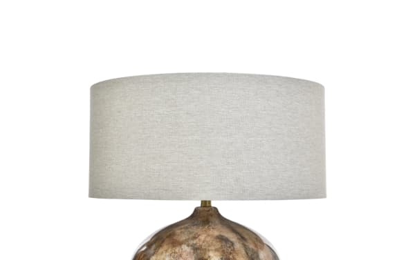 Table lamp with a beige fabric drum shade and a rounded, metallic bronze base with a textured finish, suitable for home or office decor.