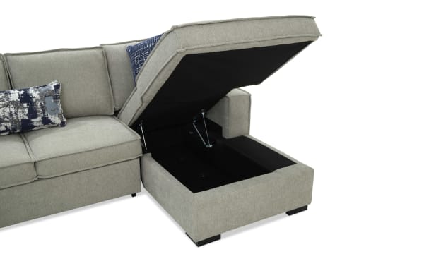 Gray fabric sectional sofa with storage chaise featuring a lift-up seat revealing black interior storage space and decorative blue and gray pillows.
