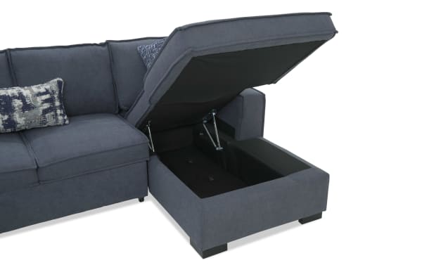 Dark gray fabric sectional sofa with storage compartment under the chaise lounge, featuring metal hinges and decorative blue patterned pillows.