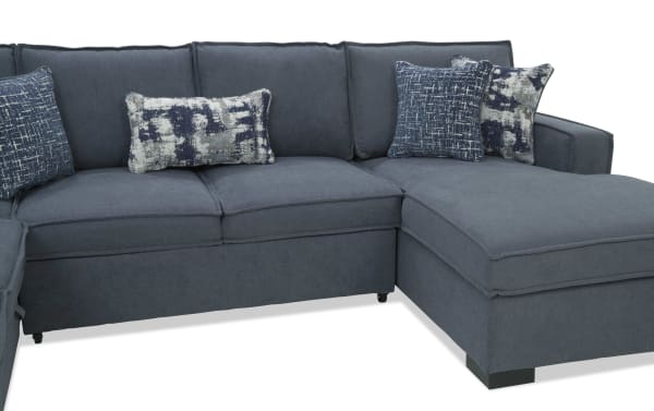 Dark blue fabric sectional sofa with chaise lounge, featuring plush cushions and patterned blue and white throw pillows, modern design.