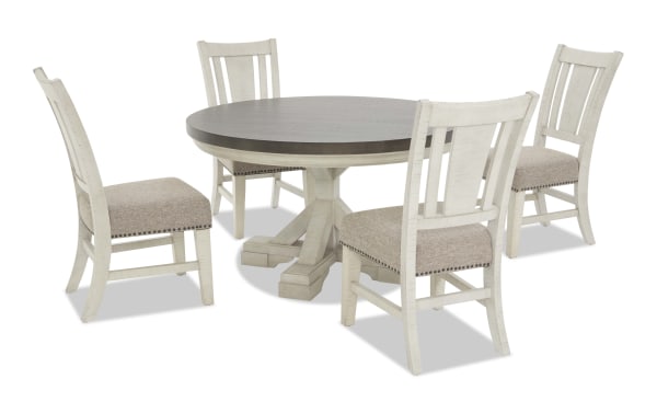 Round dining table set with a dark wood top and white distressed pedestal base, paired with four white wooden chairs featuring beige upholstered seats and nailhead trim.
