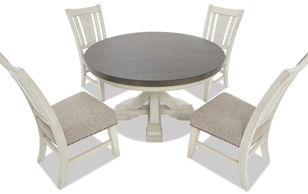 Round dining table set with a dark wood tabletop and white distressed wooden base, paired with four white wooden chairs featuring beige upholstered seats and nailhead trim.