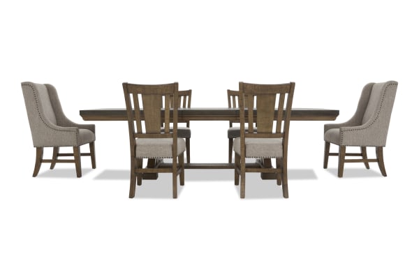 Dining set with a rectangular wooden table and six chairs, featuring beige upholstered seats and backs with nailhead trim, rustic style.