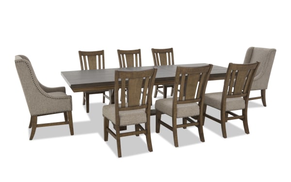 Rectangular dark wood dining table set with eight chairs, featuring beige upholstered seats and backs, nailhead trim, and a mix of high-back armchairs and side chairs.
