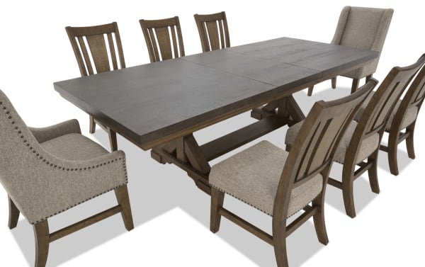 Extendable rectangular dining table with dark wood top and trestle base, paired with six wooden chairs and two beige upholstered armchairs with nailhead trim.