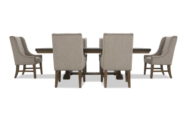 Rectangular dark wood dining table with six beige upholstered chairs featuring nailhead trim and wooden legs, suitable for formal dining rooms.