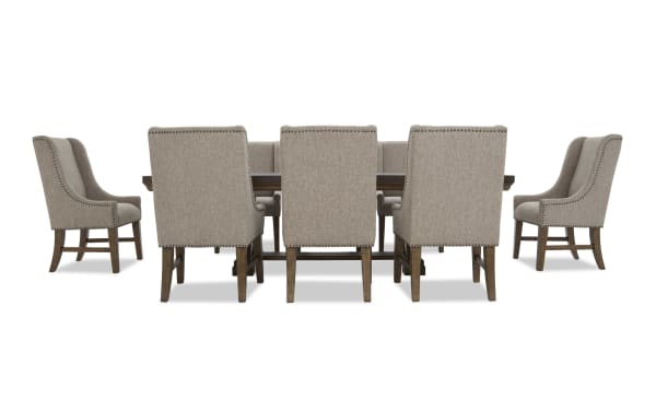 Dining set with eight beige upholstered chairs featuring nailhead trim and wooden legs, paired with a dark wood rectangular table.