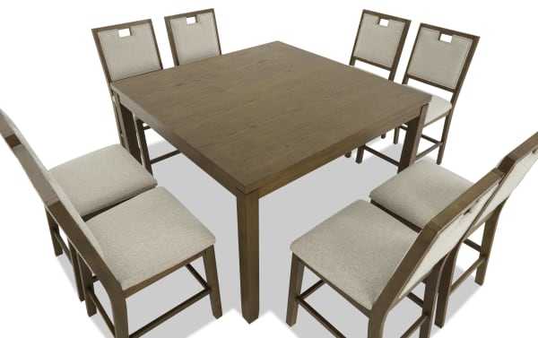 Square wooden dining table with a medium brown finish, paired with eight cushioned chairs featuring beige fabric upholstery and wooden frames.
