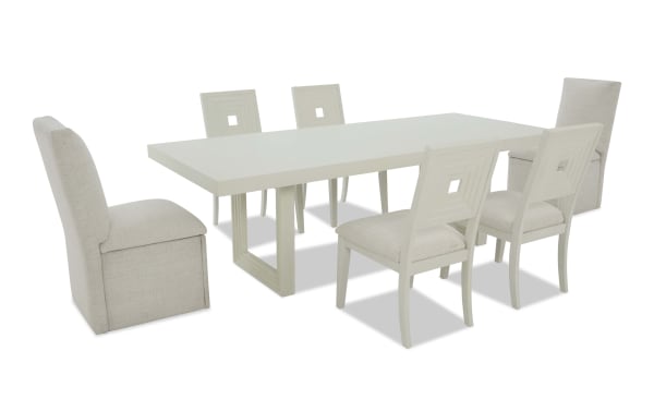 Modern rectangular white dining table set with six beige fabric-upholstered chairs, featuring wooden legs and geometric backrest design.