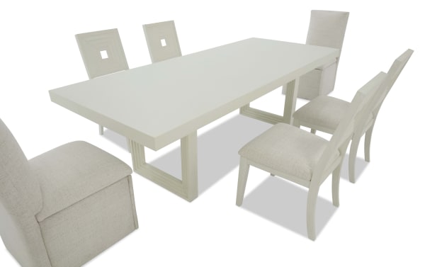 White modern dining table set with six upholstered chairs, featuring a rectangular wooden table and cushioned seats in light beige fabric.