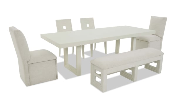Modern white dining set featuring a rectangular table with geometric leg design, two armless chairs, two square-back chairs, and a cushioned bench with light fabric upholstery.