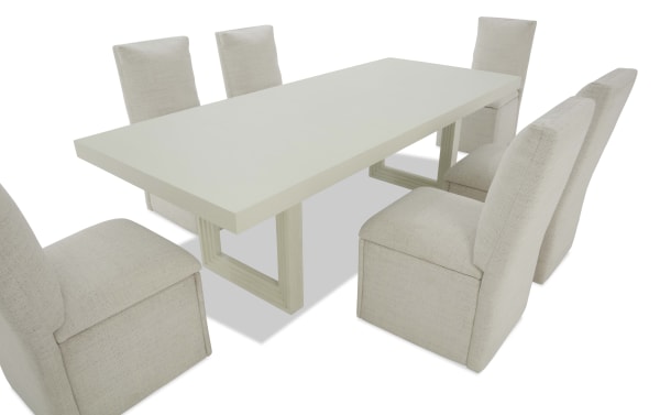 Rectangular modern dining table with a smooth white wood finish and six beige upholstered high-back chairs, featuring a minimalist design.