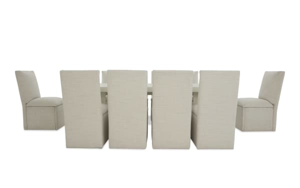 Beige upholstered dining chairs with high backs arranged around a rectangular white dining table, showcasing modern fabric seating for eight.
