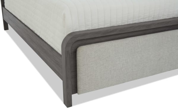 Modern bed frame corner with gray wood finish and upholstered beige fabric panel, showcasing contemporary bedroom furniture design and materials.