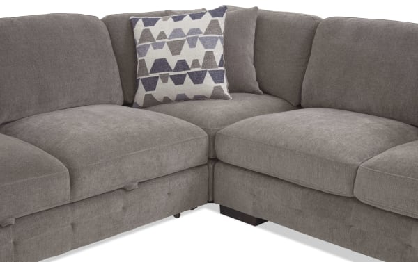 Section of a gray fabric sectional sofa with plush cushions and two decorative pillows, one with a geometric pattern in shades of blue and gray.