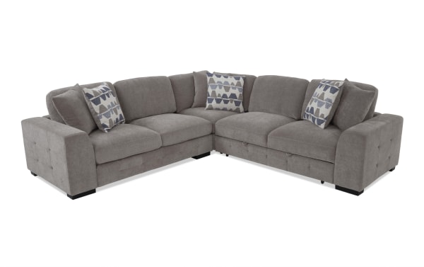 Gray fabric sectional sofa with tufted armrests, plush cushions, and geometric patterned throw pillows, designed for modern living rooms.
