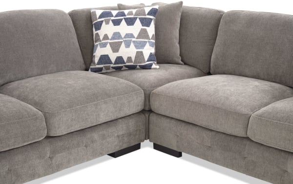 Section of a modern gray fabric sectional sofa with plush cushions and two decorative pillows, one with blue and gray geometric patterns, designed for comfortable living room seating.