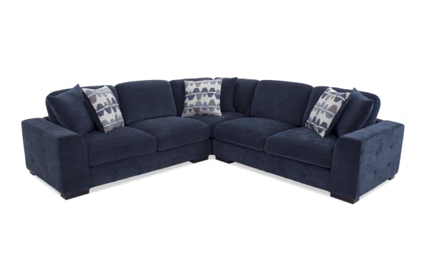 Dark blue velvet sectional sofa with tufted armrests, thick cushions, and three patterned accent pillows, ideal for modern living rooms.