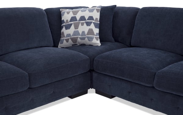 Dark blue fabric sectional sofa with plush cushions and a patterned gray and blue throw pillow, showcasing modern comfort and style.
