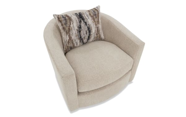 Beige upholstered swivel armchair with rounded back and sides, featuring a textured fabric and a decorative patterned throw pillow.