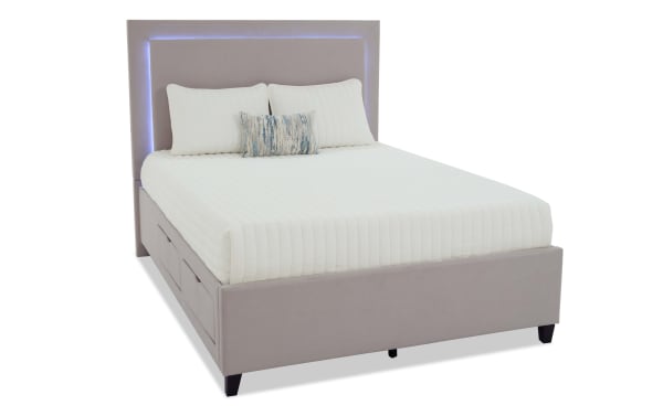 Modern upholstered bed with light gray fabric, tufted headboard featuring built-in LED lighting, and white quilted bedding with decorative pillows.