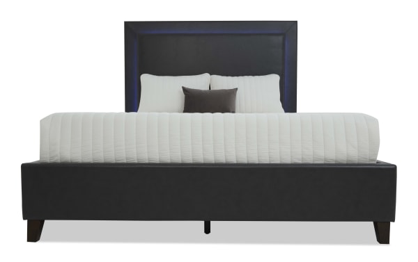 Modern black upholstered bed frame with padded headboard featuring subtle blue LED lighting, dark wooden legs, and white quilted bedding.