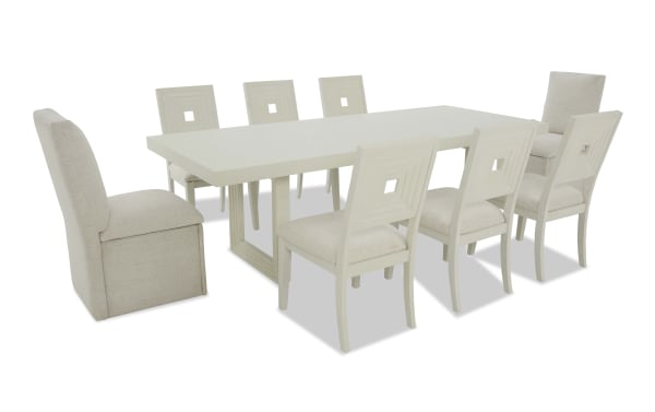 Modern white rectangular dining table set with eight beige upholstered chairs, featuring geometric cutout backrests and cushioned seats.