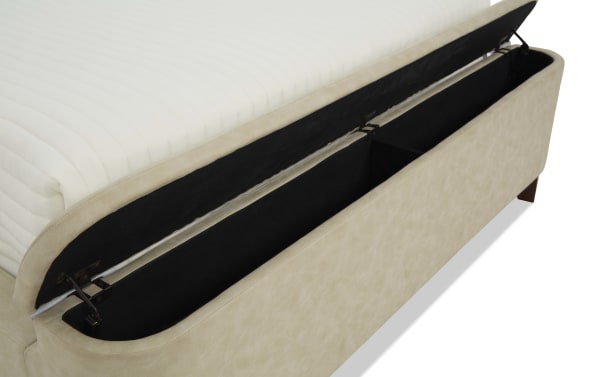 Beige upholstered storage bed base with lift-up mattress platform revealing spacious black fabric-lined storage compartment, ideal for bedroom organization.