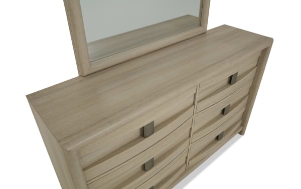 Light wood dresser with six curved front drawers and dark metal handles, topped with a matching framed mirror, showcasing modern bedroom furniture design.