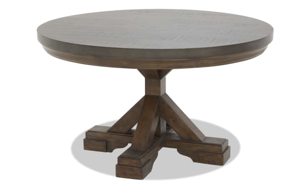 Round wooden dining table with a dark brown finish, featuring a sturdy pedestal base with four thick legs and rustic detailing.