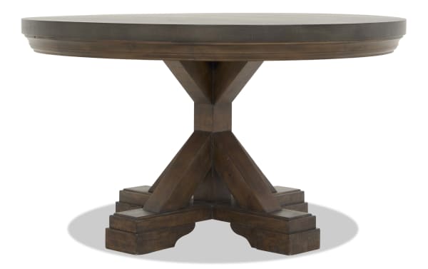 Round wooden dining table with dark brown finish, thick pedestal base with cross supports, rustic farmhouse style.