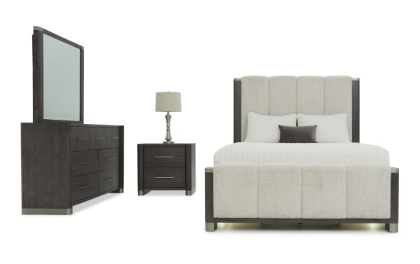 Modern bedroom set featuring a dark wood dresser with mirror, matching nightstand with lamp, and a beige upholstered bed with padded headboard and footboard.