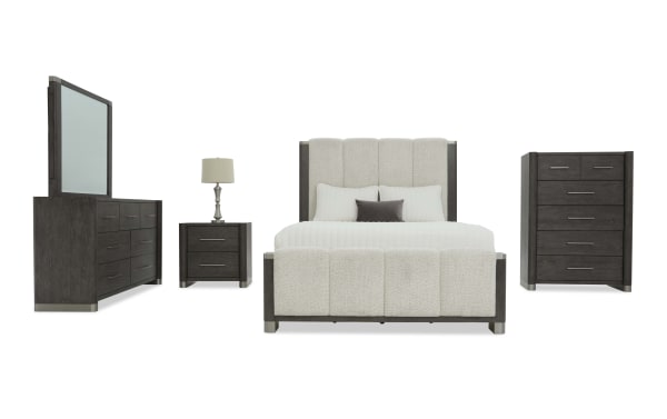 Modern bedroom furniture set featuring a dark wood finish with metal accents, including a tufted upholstered bed with cream fabric, matching dresser with mirror, nightstand with lamp, and tall chest of drawers.