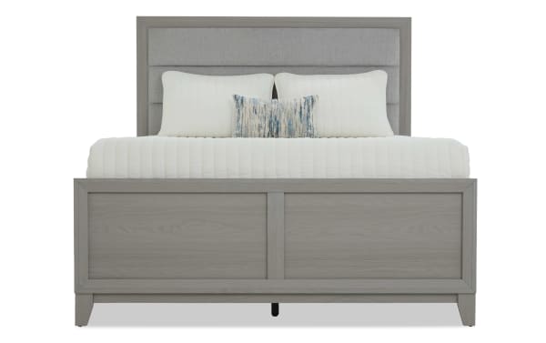Gray wooden bed frame with a paneled headboard and footboard, styled with white bedding and decorative pillows, showcasing modern bedroom furniture.