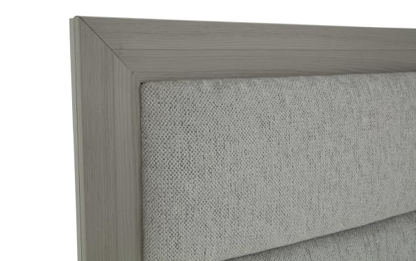 Close-up of a gray fabric upholstered headboard with a light wood frame, showcasing textured woven material and clean corner detailing.