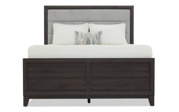 King-size bed with dark wood frame, upholstered gray fabric headboard, white bedding, and decorative blue-gray accent pillow.