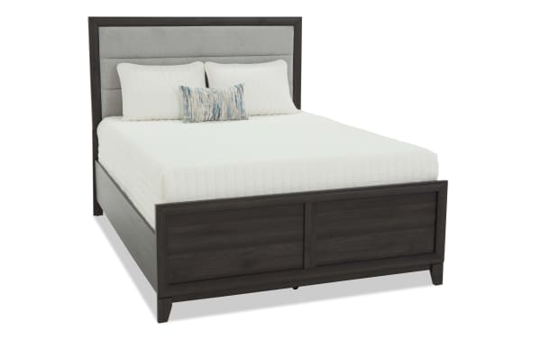 Queen-size bed with dark wood frame, gray upholstered headboard, white quilted bedding, and decorative pillows, modern style.